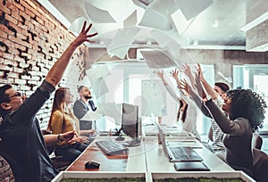 Group of young business people throwing documents and looking happy while celebrating success at their working places in startup