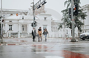 A group of young business professionals crossing a snowy city street. They are dressed warmly for the cold weather