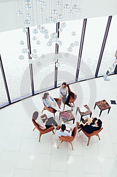 Group of young business professionals sitting together and having casual discussing in office hallway achieving goals.