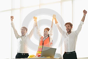 Group of young businessman and woman engineer celebrating by raised hands up to show achievement in brightness office atmosphere.