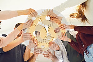 A group of young businessmen in casual clothes are holding wooden gears with their hands.