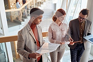 Group of young businesspeople comparing data, information, at hallway in business building