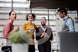 A group of young businesspeople with cup of coffee standing in office, talking.