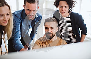 Group of young businesspeople looking at laptop screen in office, discussing issues.