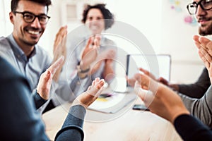 Group of young businesspeople sitting around table in a modern office, clapping.