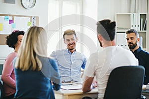 Group of young businesspeople sitting around table in a modern office, having meeting.