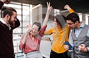 A group of young businesspeople with smartphone standing in office, expressing excitement.