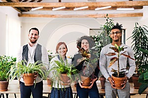 Group of young businesspeople standing in office, holding plants.