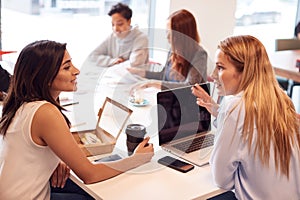 Group Of Young Businesswomen Sitting Around Table In Modern Workspace Having Working Lunch Meeting