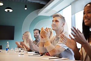 Group Of Young Candidates Sitting At Boardroom Table Applauding Presentation At Business Graduate Recruitment Assessment Day