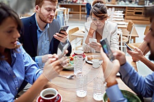 Group of young caucasian people having unsocial lunch in restaurant, using their cell phones and not talking to each other.