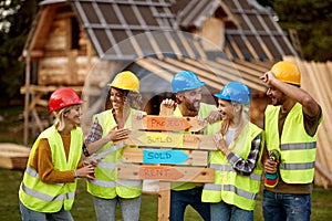 A group of young cheerful both female and male builders enjoy posing for a photo at a cottage construction site. Construction,