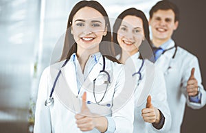 Group of young cheerful doctors is standing as a team with thumbs up in a hospital office and is ready to help patients