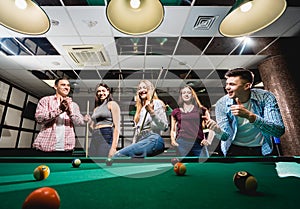 Group of young cheerful friends playing billiards.