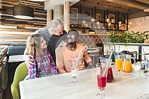 A group of young cheerful friends are sitting in a cafe, eating, drinking drinks, take selfies and take pictures