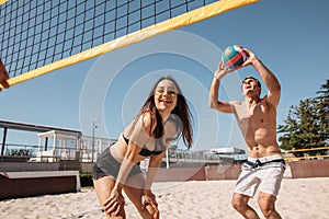 Group of young cheerful people playing beach volleyball on sunny day