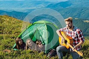 Group of young cheerful woman in camp tent together while young handsome man playing guitar.