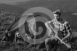 Group of young cheerful woman in camp tent together while young handsome man playing guitar.