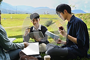 Group of young college students reading book on green lawn at campus. Youth lifestyle, university and friendship concept