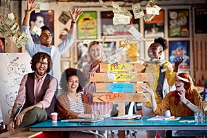 Group of young creative people are posing for a photo at their workplace while celebrating successes and throwing money around the