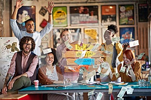 A group of young creative people are posing for a photo and throwing the money around the office celebrating a success. Employees