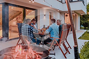 A group of young diverse people having dinner on the terrace of a modern house in the evening. Fun for friends and