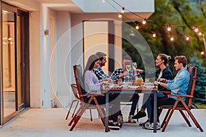 A group of young diverse people having dinner on the terrace of a modern house in the evening. Fun for friends and