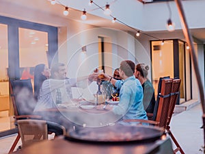 A group of young diverse people having dinner on the terrace of a modern house in the evening. Fun for friends and