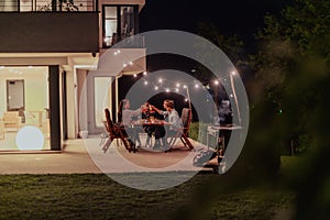 A group of young diverse people having dinner on the terrace of a modern house in the evening. Fun for friends and