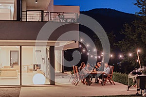 A group of young diverse people having dinner on the terrace of a modern house in the evening. Fun for friends and