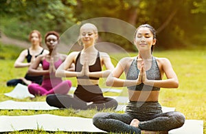 Group of young diverse women meditating in lotus pose during yoga class at park, empty space