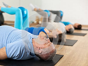 Group of young elderly people in sportswear exercising Pilates with mini balls while lying on mats in rehabilitation