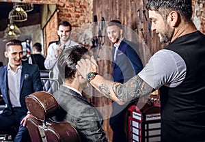 Group of young elegant positive mens pose in interior of barbershop.