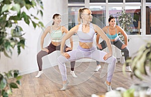 Group of young energetic women in tight activewear warming up with dancing elements before training together in fitness