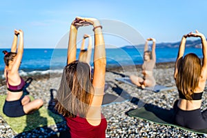 group of young females practicing yoga on the seaside