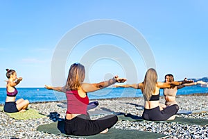 group of young females practicing yoga on the seaside