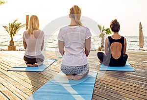 Group of young females practicing yoga on the seaside during the sunrise