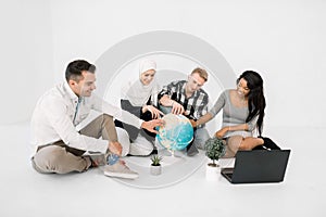 Group of young four multiethnical people, African and Muslim women, two Caucasian men, pointing at planet Earth, sitting