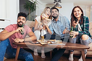 Group of young friends eating pizza and watching tv.