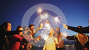 Group of young friends having a beach party. Friends dancing and celebrating with sparklers in twilight sunset