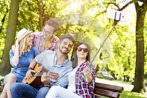 Group of young friends playing guitar and taking a selfie in a park on a sunny day