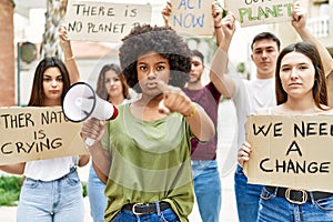 Group of young friends protesting and giving slogans at the street pointing with finger to the camera and to you, confident