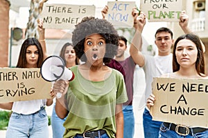 Group of young friends protesting and giving slogans at the street scared and amazed with open mouth for surprise, disbelief face