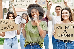 Group of young friends protesting and giving slogans at the street serious face thinking about question with hand on chin,