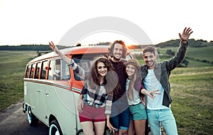 A group of young friends on a roadtrip through countryside, standing by a minivan.