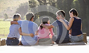 Group Of Young Friends Sitting On Wooden Jetty Looking Out Over Lake