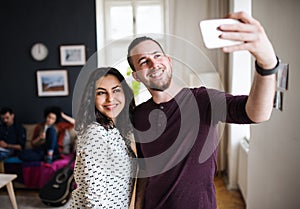 A group of young friends with smartphone indoors, taking selfie.