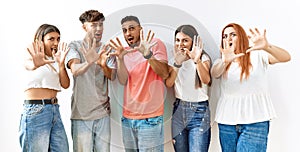 Group of young friends standing together over isolated background afraid and terrified with fear expression stop gesture with