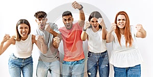 Group of young friends standing together over isolated background angry and mad raising fists frustrated and furious while