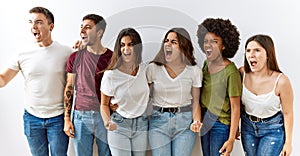 Group of young friends standing together over isolated background angry and mad screaming frustrated and furious, shouting with